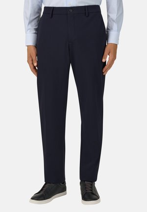 Navyfarbige Hose aus glattem Stoff, mit flachem Bund, Seitentaschen und Knopfverschluss, kombiniert mit schwarzen Sneakers.