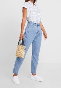 Blå- och vitrandig kortärmad skjorta, hög midja ljusblå jeans, vita sneakers och en liten vävd beige handväska med svarta handtag.