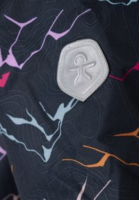 Tessuto con uno sfondo scuro caratterizzato da motivi ondulati colorati in rosa, blu e arancione. Include un'etichetta con logo esagonale in argento.