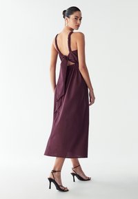 Bordo maksi obleka s halter izrezom, elastičnim pasom, odprtim hrbtom, zavezanim z mašno in gladkim materialom. Uparjena s črnimi sandali na višji peti.