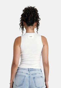 Top de tirantes blanco con cuello redondo, diseño ajustado. Presenta una pequeña etiqueta de la marca en la parte de atrás, combinado con unos jeans de tiro alto azul claro.