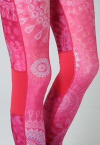 Leggings rosa con motivo caratterizzati da disegni intricati in rosa chiaro, pannelli laterali rossi in contrasto e dettagli testurizzati per una maggiore aderenza.