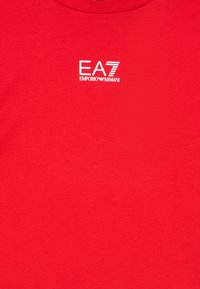 Rdeča bombažna majica s krožnim izrezom in belim tiskanim logotipom "EA7 Emporio Armani" na prsih. Gladek tekstura, priložnostna zasnova.
