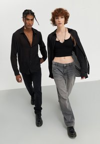 Svartstripete gjennomsiktig skjorte med knapper, svarte jeans, svarte støvler; cropped svart tank-top, grå jeans, svartstripet oversized skjorte.