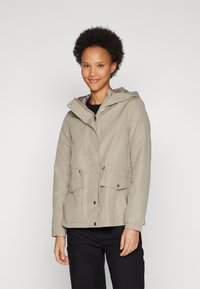 Beige lett jakke med hette, snøring i midjen og to frontlommer; glatt tekstur med et uformelt design og elastiske mansjetter.
