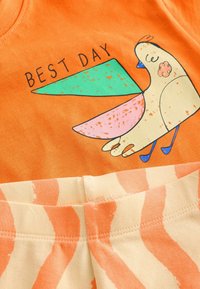 Orange bomulds t-shirt med et fugletryk i grønne og pink nuancer. Teksten "BEDSTE DAG" er trykt over designet.