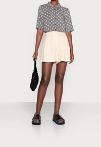 Koszula z krótkim rękawem w biało-czarny wzór, beżowe spodenki z plisami, czarna torebka o fakturowanej powierzchni oraz czarne sandały na platformie z detalami na paskach.