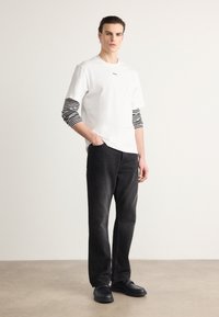 T-shirt blanc à manches courtes sur une chemise à manches longues rayée noir et blanc, associé à un jean foncé et des chaussures noires à enfiler.