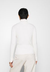 Maglione bianco a collo alto con maniche lunghe, design aderente e leggero texture, mostrato da dietro su uno sfondo neutro.