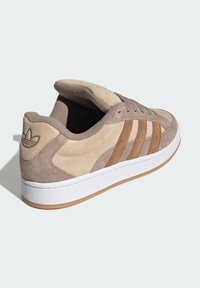 Beige nubuck sneakers med brune accenter, tre striber, hvid gummisål og prægede logo på hælen. Rundet tå og polstret krave.