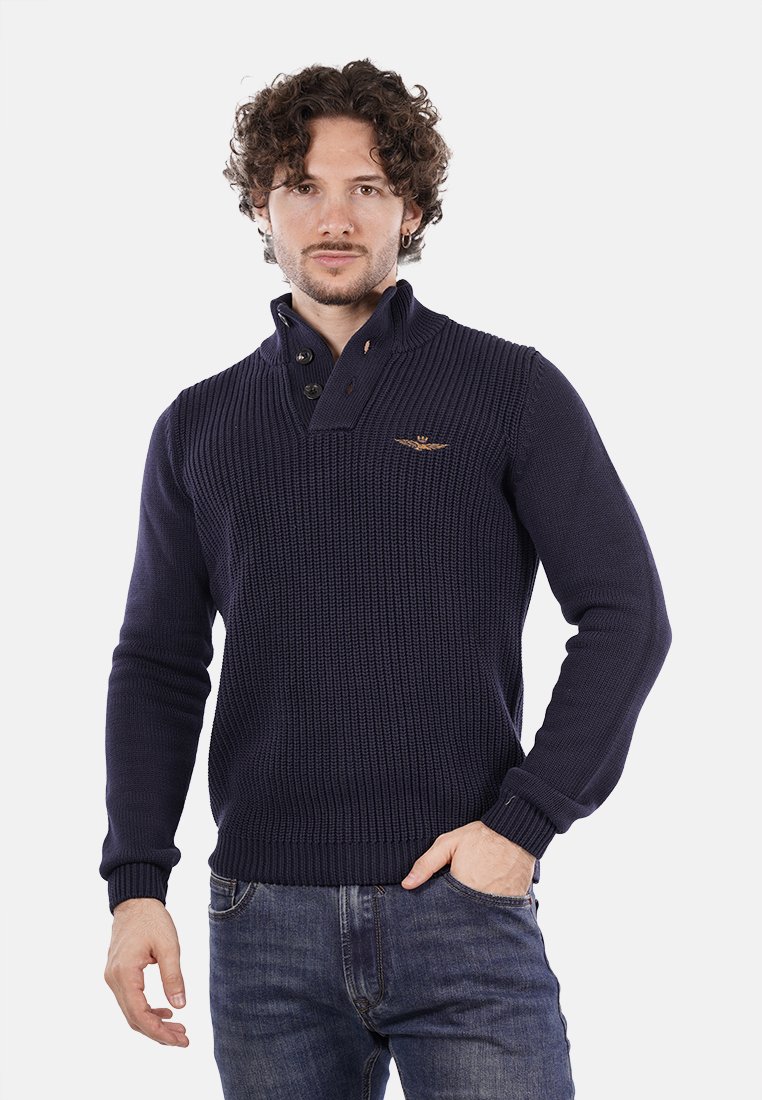 Pullover lavorato a maglia di colore blu navy con colletto alto, due bottoni e texture a coste. Presenta un piccolo logo sul petto a sinistra. Abbinato a jeans.