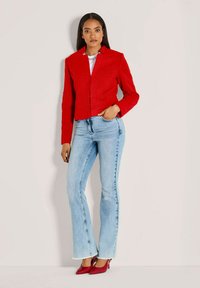 Rote, gesteppte, kurze Jacke mit Reverskragen, kombiniert mit hoch taillierten, hellblauen Schlagjeans und roten Pumps.