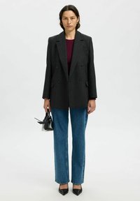 Oglata dvoredna blazer v ogljeni barvi, v kombinaciji z maroon vrhom, modrimi naravnost krojenimi kavbojkami in črnimi čevlji s koničastim noskom. V roki majhna črna torbica.