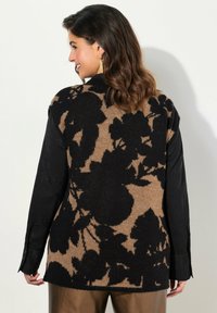 Strickcardigan mit einem schwarz-beigen Blumenmuster, einem gepolsterten schwarzen Stoff vorn und einem strukturierten Strickrücken, langen Ärmeln und einem lockeren Schnitt.