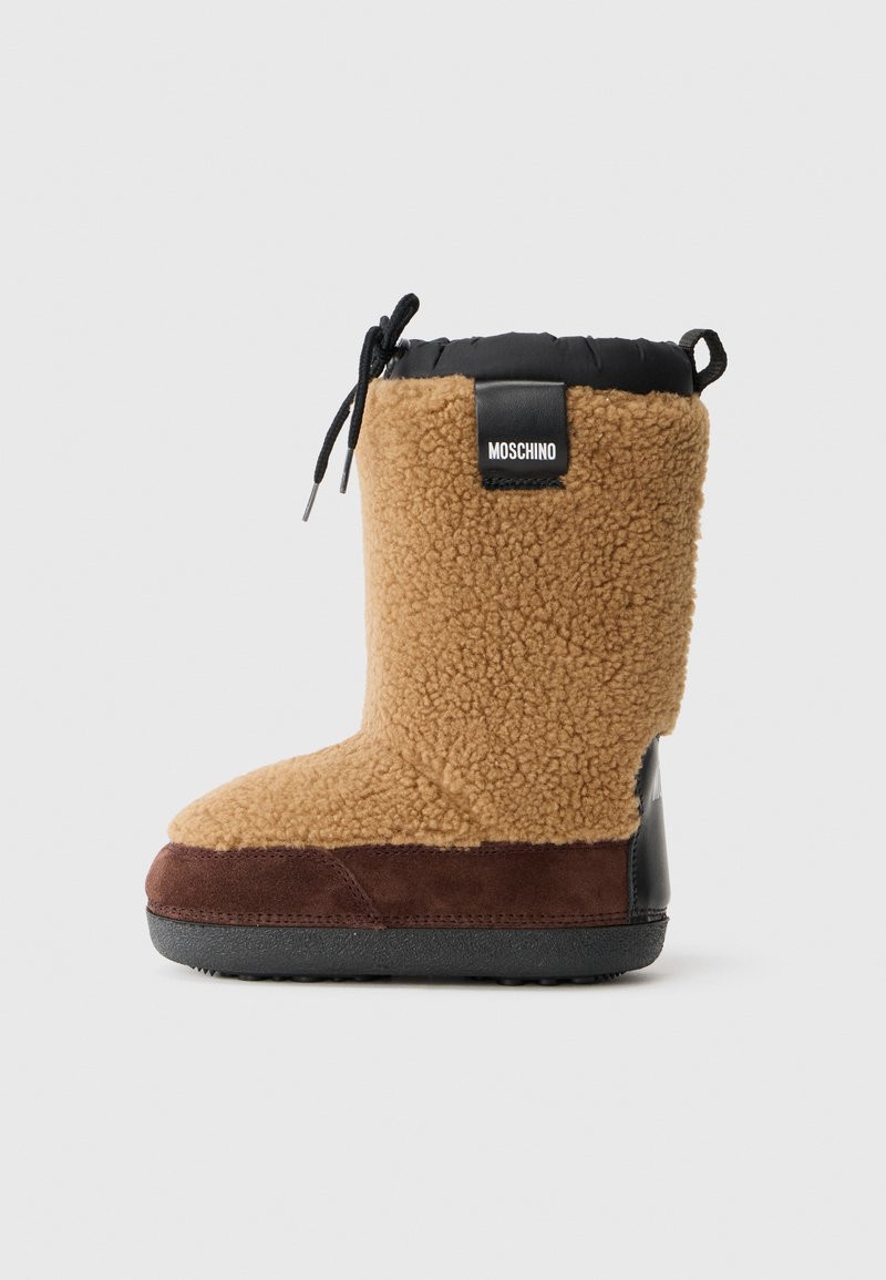 Bottes en fourrure de couleur beige avec un dessus en nylon noir, un accent en daim marron et une semelle en caoutchouc texturée ; elles sont dotées d'un système de fermeture à cordon et d'un logo à l'arrière.