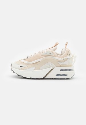 Baskets Nike beige et blanches avec une semelle épaisse et un détail de coussin d'air visible, vues de profil sur un fond blanc uni.