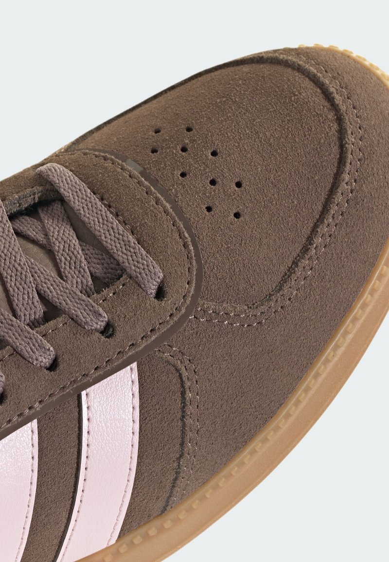 Brauner Wildledersneaker mit rosafarbenen Lederstreifen, runder Spitze, Perforationen am Vorderblatt und einer Kautschuksohle in Kaugummifarben. Flache Schnürsenkel und Ziernähte.