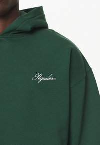 Felpa verde realizzata in morbido cotone, con cappuccio regolabile e logo "Pegador" ricamato in bianco nella zona del petto.