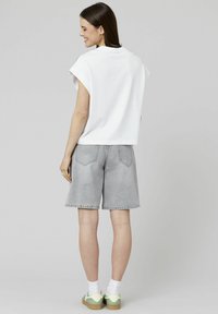 Haut en coton blanc à manches courtes associé à un short en denim gris, affichant une coupe décontractée et des détails de poche classiques, porté avec des baskets basses.