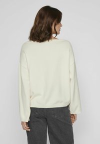 Pull en crème à coupe ample, épaules tombantes et ourlet côtelé. Associé à un jean taille haute gris foncé à jambes larges, vu de l'arrière.