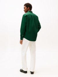 Grünes Langarmhemd mit Kragen und Knopfmanschetten. Kombiniert mit weißen Hosen und schwarzen Schuhen. Glatte Textur, taillierte Passform.