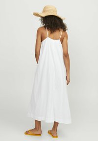 Vestido maxi blanco sin mangas, con un corte holgado y tirantes finos. Se lleva con chanclas amarillas y un sombrero de paja, con una tela texturizada.