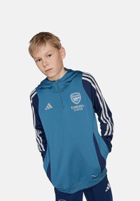 Adidas Arsenal hoodie in blauw met witte strepen, voorzien van logo, ritssluiting vooraan en zakken. Zachte, ademende stof.