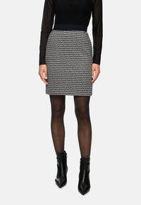 Black and white patterned fitted skirt with a solid waistband, paired with sheer black tights and high-heeled black ankle boots.