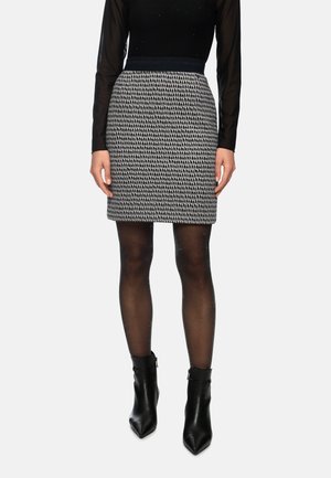 Schwarz-weiß gemusteter enger Rock mit einem einfarbigen Bund, kombiniert mit transparenter schwarzer Strumpfhose und hohen schwarzen Stiefeletten.