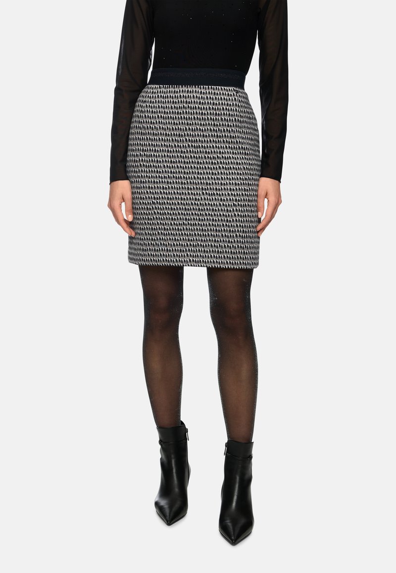 Black and white patterned fitted skirt with a solid waistband, paired with sheer black tights and high-heeled black ankle boots.