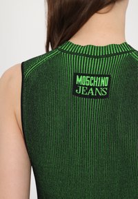 Zöld bordázott ujjatlan póló fekete részletekkel és Moschino Jeans logóval a hátsó részen. Texturált, testhez álló kialakítással rendelkezik.