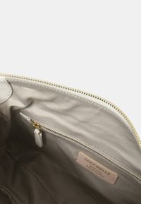 Interno della borsa a tracolla in pelle beige con tasca con zip e etichetta di marca. Texture liscia e morbida con zip dorata e fodera.
