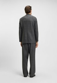 Completo grigio a quadri con giacca su misura e pantaloni plissettati. Realizzato in tessuto testurizzato, presenta una vestibilità classica e linee di design sobrie.