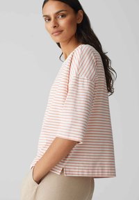 Gestreiftes Baumwolloberteil mit korallfarbenen und weißen Linien, weiten Ärmeln, rundem Halsausschnitt und einem leichten Schlitz am Saum. Weicher Stoff, lockere Passform.
