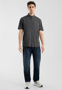 Camisa de botones de manga corta en color carbón con un patrón texturizado, combinada con jeans azul oscuro y zapatillas blancas.