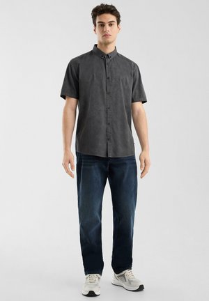 Camisa de botones de manga corta en color carbón con un patrón texturizado, combinada con jeans azul oscuro y zapatillas blancas.