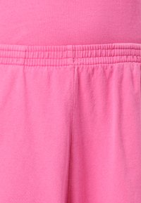 Tuva roza elastīgā jostas vieta uz mīkstiem auduma biksēm vai šortiem ar vertikālu šuvuma detaļu centrā.