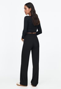 Zwarte lange mouwen crop top gecombineerd met wijde zwarte broek, beide gemaakt van zachte stof. De broek heeft een soepele elastische tailleband.