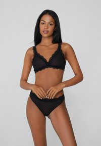 Conjunto de lencería negra que incluye un bralette con estampado de lunares y borde de encaje, combinado con braguitas de talle alto a juego. Textura transparente.