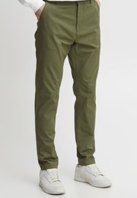 Olivenfargede, lette bukser med rett snitt, som har knapp- og glidelåslukking, samt to sidelommer. Bært med hvite sneakers.
