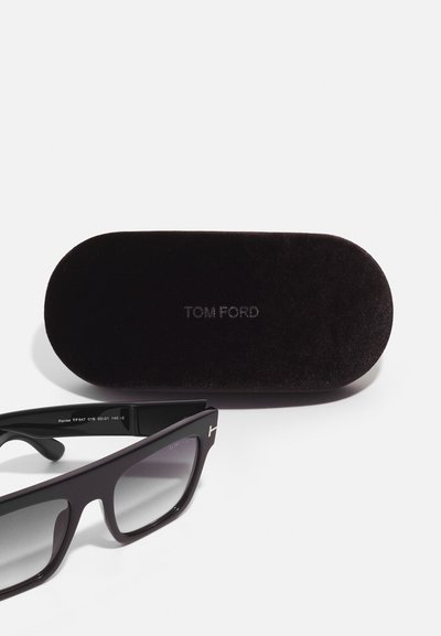 Ochelari de soare negri cu lentile degradate, având un râmă groasă și accente de aur. Însoțiți de un toc de catifea întunecată, gravat cu "TOM FORD."