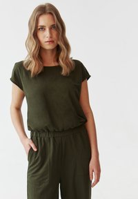 Top scurt de culoare verde închis, cu guler rotund și croi lejer, asortat cu pantaloni cu talie înaltă, care au buzunare laterale.
