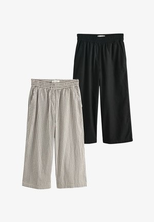 Zwei Paare von gekürzten Hosen mit elastischem Bund, einfarbig schwarz und schwarz-weiß kariert, flach auf einem weißen Hintergrund liegend dargestellt.