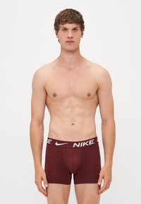 Herre burgunderfarvede boxer briefs med et hvidt Nike-logo på det elastiske bæltedesign. Glat stof med en tætsiddende pasform og længde til midt på låret.