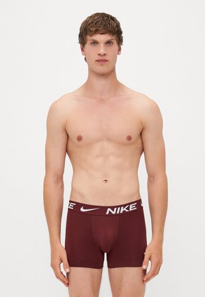 Männliche bordeauxfarbene Boxershorts mit einem weißen Nike-Logo auf dem elastischen Bund. Glattes Material mit enganliegendem Design und mittellanger Beinform bis zum Oberschenkel.