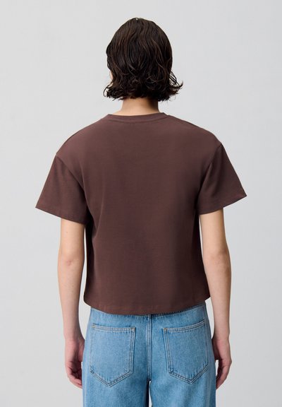 T-shirt cropped marron à manches courtes, fabriqué en coton doux. Son design décontracté présente un col rond et un minimalisme dans les détails. Assorti à un jean bleu taille haute.
