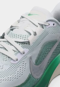 Chaussure de course Nike blanche et verte avec dessus en mesh, lacets blancs et logo Nike argenté réfléchissant sur le côté.