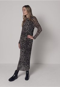 Robe à manches longues en tissu transparent à imprimé léopard, avec une silhouette droite et un léger éclat, associée à des bottines noires.