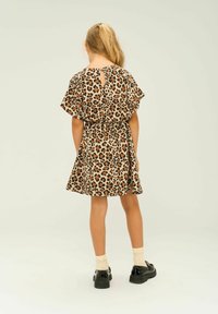 Klänning med leopardmönster, korta fladderärmar, smal midja och utfläkt kjol. Nyckelhålsdetalj på baksidan och svarta skor synliga.