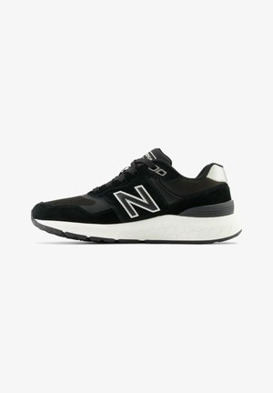 Chaussures de sport noires avec un dessus en maille et en daim, présentant un logo blanc et une semelle intermédiaire texturée blanche avec une semelle extérieure en caoutchouc noir.
